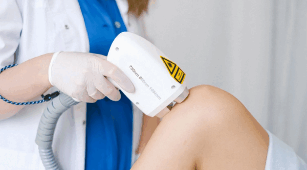 Doctor administering laser therapy session to patient's knee.
